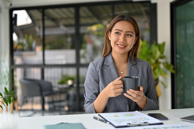 Charmante asiatische Geschäftsfrau, die entspannt Kaffee trinkt und von ihrem beruflichen Erfolg träumt