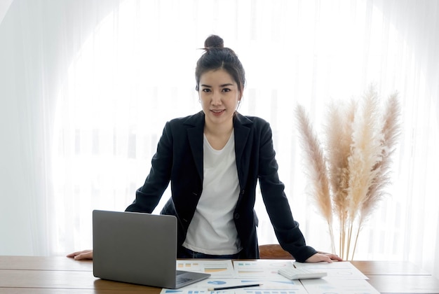 Charmante asiatische Geschäftsfrau mit einem Lächeln, die klug im Büro steht und in die Kamera schaut