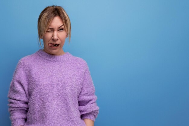 Charmante blonde junge tausendjährige Frau im lässigen Look macht eine Grimasse auf hellem Hintergrund mit