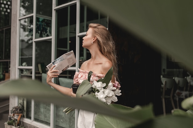 Foto charmante blondine mit einem strauß weißer blumen und einer zeitung in der hand