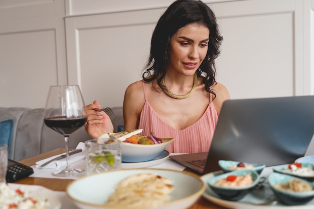 Charmante brünette Dame, die sich Videos auf dem Notebook ansieht und beim Mittagessen im Café lächelt