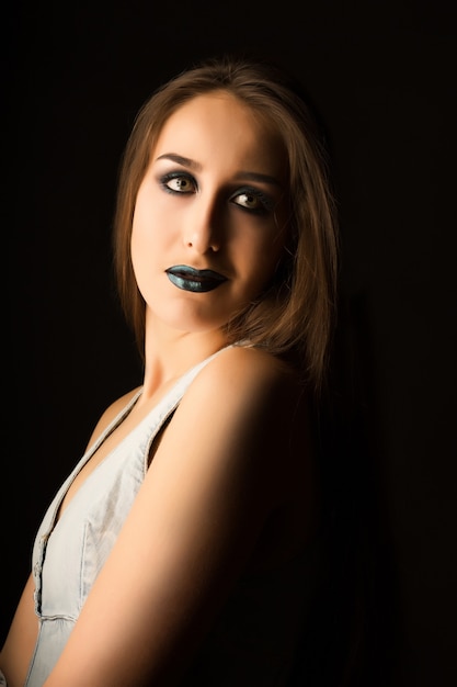 Charmante brünette Frau mit perfekter Haut und kreativem metallisch-grünem Make-up. Nahaufnahmeportrait im Studio auf dunklem Hintergrund