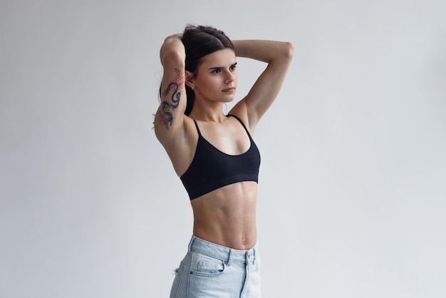 Charmante, dünne, schöne Mädchen mit perfekten Bauchmuskeln in Jeans und schwarzem Oberteil, isoliert auf hellem Hintergrund