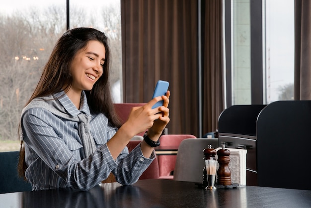 Charmante Frau mit schönem Lächeln, die gute Nachrichten auf dem Handy während der Ruhe im Café liest, glückliche kaukasische Frau, die ihre Fotos auf dem Handy beim Entspannen im Café während der Freizeit beobachtet