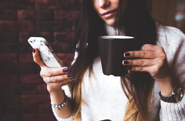 Charmante Frau schaut am Telefon im Café. Leckerer Schokoladenkuchen und Kaffee auf dem Tisch.