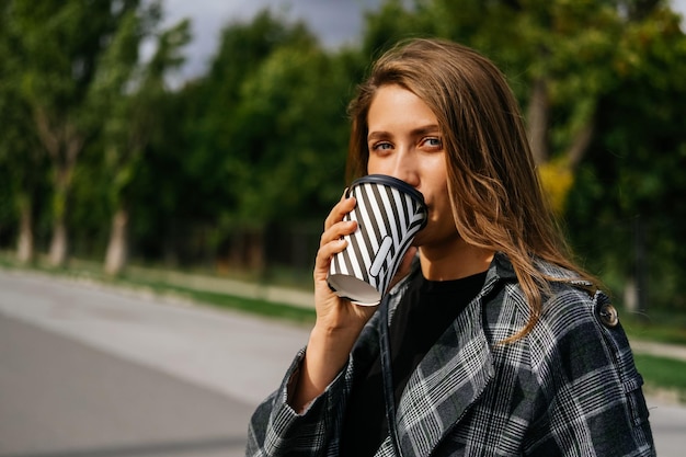 Charmante Frau trinkt einen guten Kaffee zum Mitnehmen, während sie in die Kamera schaut