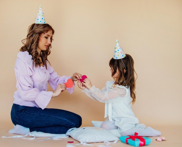 Charmante, fröhliche Familie, die auf dem Boden sitzt und sich während der festlichen Zeit amüsiert Geburtstagskonzept Mutter und Tochter gratulieren sich gegenseitig