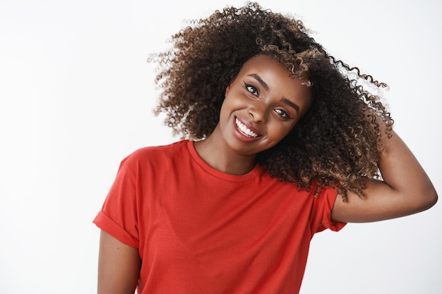 Charmante, fröhliche und süße afroamerikanische Frau mit lockigem Afro-Haarschnitt, die die Hand hinter dem kippenden Kopf hält