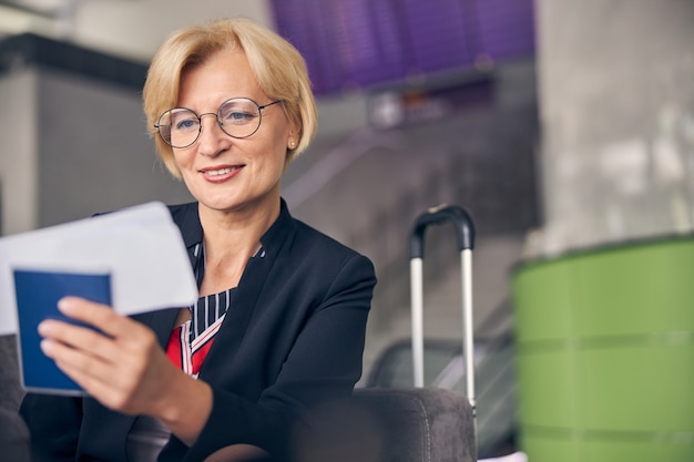 Charmante Geschäftsfrau, die auf die Bordkarte schaut und lächelt, während sie auf ihren Flug wartet?