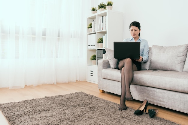 charmante Geschäftsfrau mit dem Notebook nach der Arbeit auf dem Sofa zu Hause sitzen