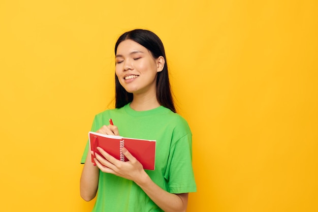 Charmante junge Asiatin grüne T-Shirts mit rotem Notizbuch und Stift isolierter Hintergrund unverändert