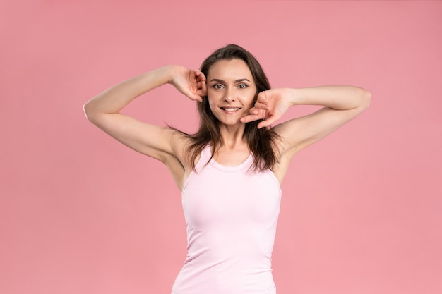 Charmante junge Frau, die Hände ohne Make-up, Hautpflegekonzept, attraktives brünettes Mädchen im rosa T-Shirt hochhält.