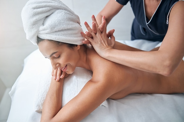 Charmante junge Frau, die Rückenmassage im Spa-Salon genießt?