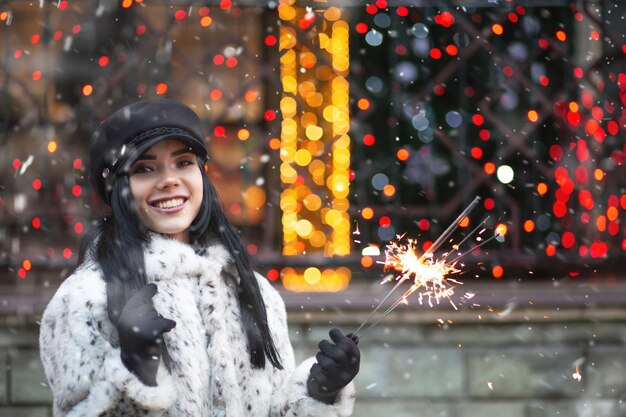 Charmante junge Frau, die Winterferien mit funkelnden Lichtern genießt. Freiraum