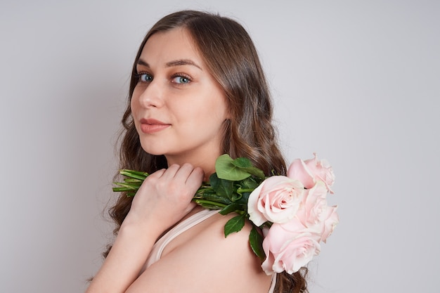Charmante junge Frau mit einem Strauß rosa Rosen auf der Schulter.