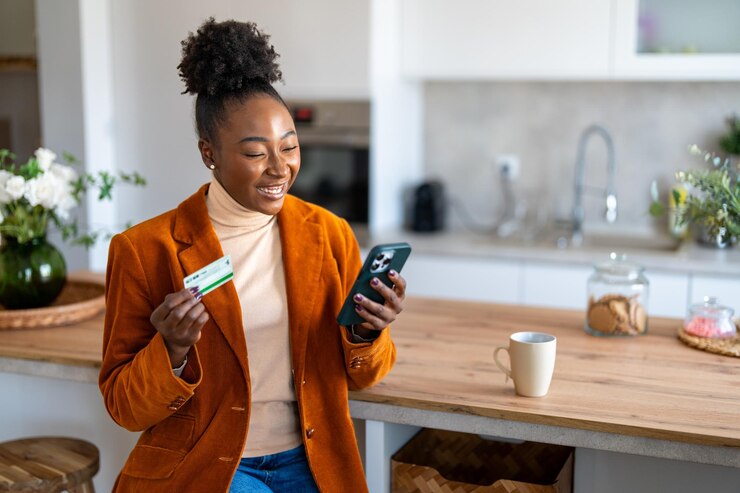 Foto charmante junge schwarze frau, die auf den smartphone-bildschirm schaut und eine kreditkarte in der hand hält, benutzt eine gesicherte online-e-banking-app mit handy und ist mit guten elektronischen bankdienstleistungen zufrieden