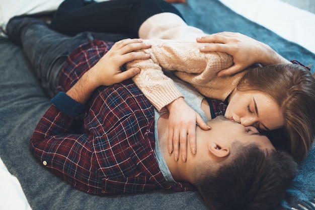 Foto charmante kaukasische frau, die mit ihrem geliebten im bett liegt, während sie sich umarmt und küsst