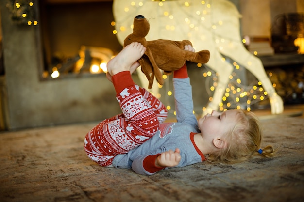 Charmante kleine Blondine auf dem Teppich im Haus dekoriert für Weihnachten. Gemütliche Weihnachten