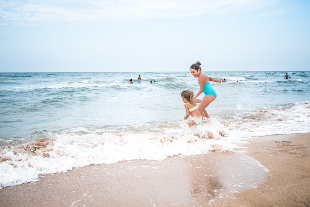 Charmante kleine Mädchen Schwestern schwimmen und planschen in den Wellen des Meeres an einem sonnigen heißen Sommertag während der Ferien