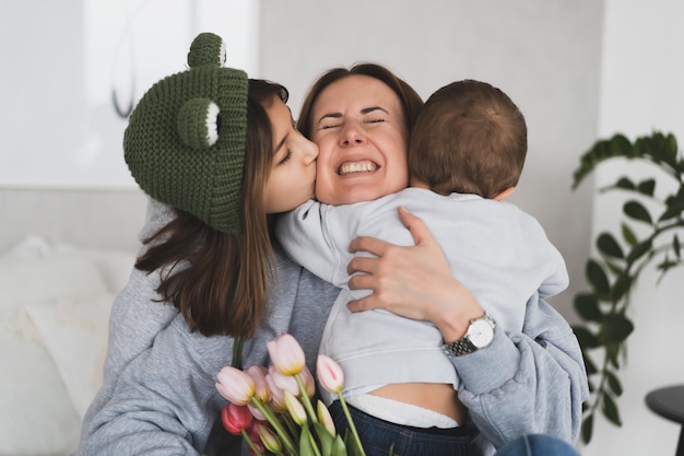 Charmante Mutter mit einem Strauß Tulpen und ihre Kinder Tochter und kleiner Sohn haben Spaß zu Hause
