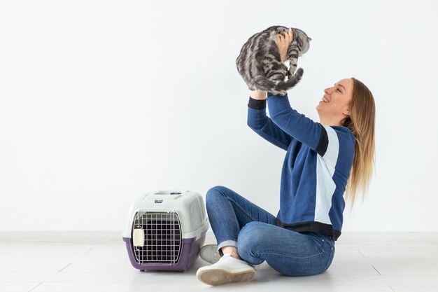 Charmante positive junge Frau hält in ihren Händen ihre schöne graue Falte schottische Katze, die auf dem Boden in einer neuen Wohnung sitzt. Haustierkonzept. Copyspace