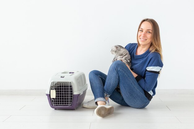 Charmante positive junge Frau hält in ihren Händen ihre schöne graue Falte schottische Katze, die auf dem Boden in einer neuen Wohnung sitzt