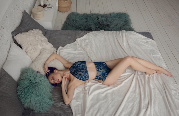 Charmante sexy Frau in Dessous, die auf dem Bett im Zimmer liegt, lila Haare und dunkelblaue Unterwäsche