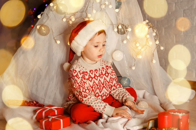 Charmanter Junge, der am Weihnachtstag mit Geschenken auf dem Boden spielt