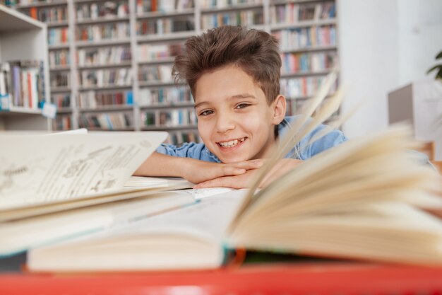 Charmanter Junge, der lächelnd in der Bibliothek ruht, nachdem er gelesen und studiert hat