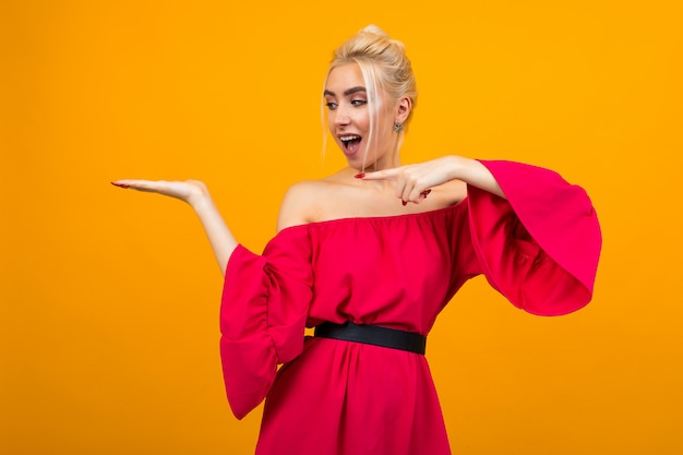 Charmantes blondes Mädchen in einem roten Kleid mit Händchenhalten an einer gelben Wand