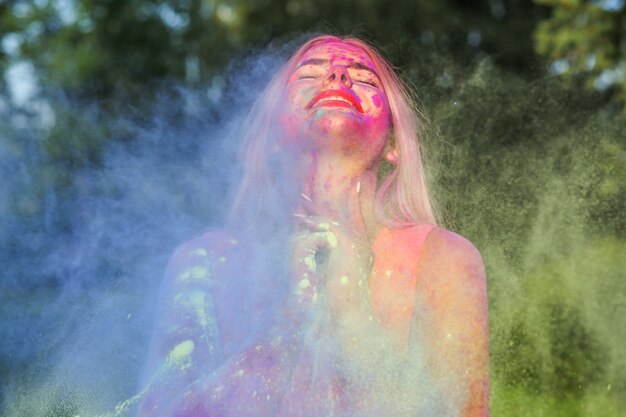 Charmantes blondes Model mit explodierender bunter Farbe, das das Holi-Festival feiert