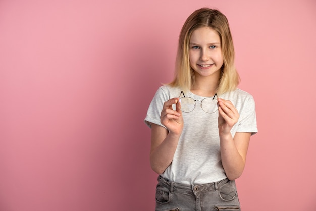 Charmantes, hübsches Mädchen mit Brille in den Händen posiert auf einer leeren Wand