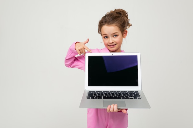 charmantes junges Mädchen in einem rosa Anzug zeigt einen Laptop-Bildschirm mit einem Layout auf einer weißen Wand