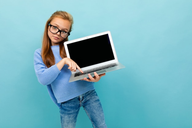 Charmantes kaukasisches Mädchen arbeitet oder studiert mit Laptop und zeigt es isoliert auf blau