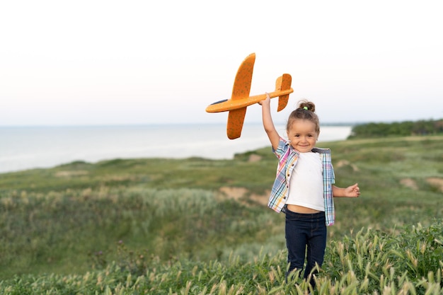 Charmantes kaukasisches Mädchen geht im Sommer auf einem grünen Feld spazieren, startet ein Flugzeug in den Himmel und träumt vom Fliegen Kindergesundheits-Lifestyle-Konzept Porträt eines Kindes in der Natur