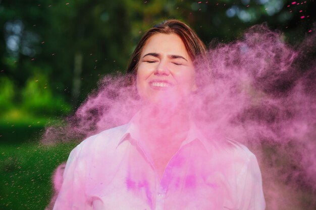 Charmantes kaukasisches Model posiert mit geschlossenen Augen und explodiert um rosa Holi-Farbe