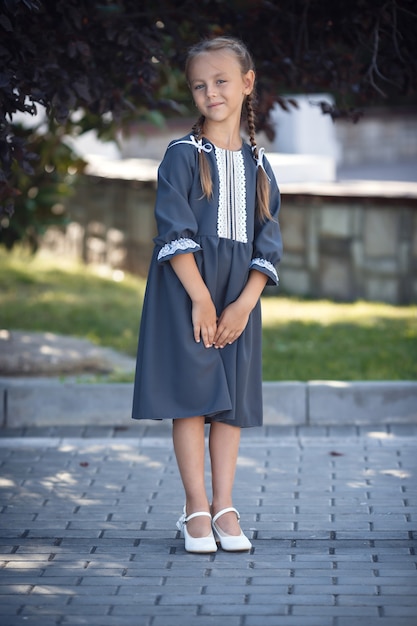 Charmantes kleines Mädchen in einem Retro-Kleid, das in der Stadt an einem sonnigen Sommertag geht. Kleines Mädchen tragen Schuluniform.