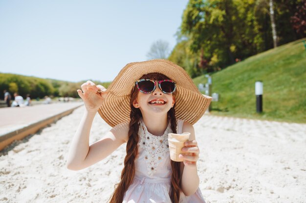 Charmantes kleines Mädchen mit Hut isst Eis am Strand Sommerurlaubskonzept