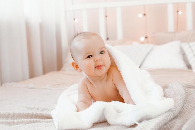 Charmantes lächelndes baby in einem handtuch, das nach dem baden auf dem bett liegt