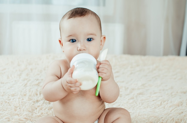 Charmantes Mädchen, das allein eine Mischung aus Milch isst, Haferbrei hält einen Löffel sitzend