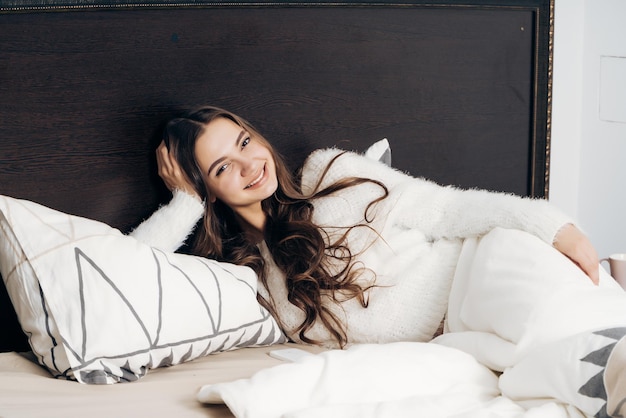 Charmantes Mädchen mit langen Haaren ruht sich abends unter einer weißen Decke im Bett aus