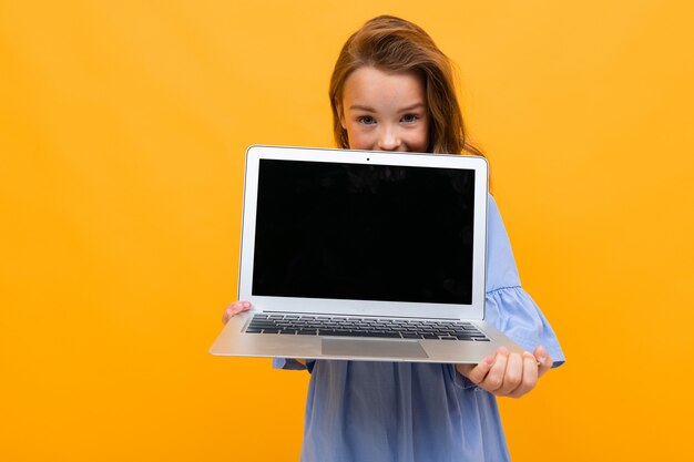 Charmantes Mädchen späht auf einen Laptop mit einem Modell an einer orangefarbenen Wand