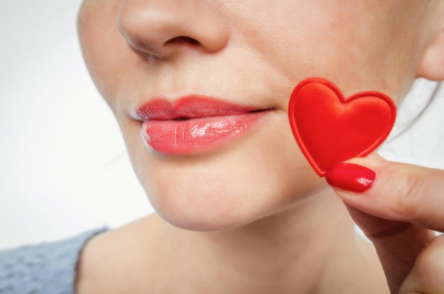 Charmantes weibliches Lächeln Weibliche Finger mit roten Nägeln halten ein kleines rotes Herz in der Nähe ihrer Lippen