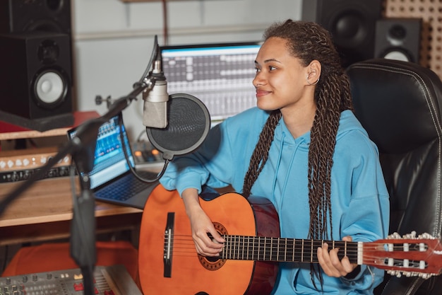 Foto charmosa e talentosa guitarrista africana adolescente gravando nova música no estúdio de música de transmissão e gravação de som