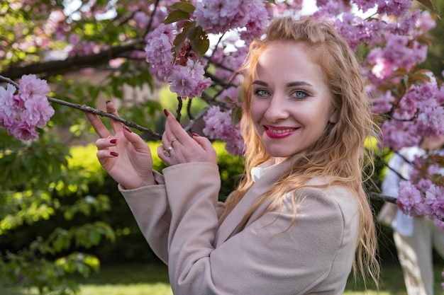 Charmosa garota à moda no parque de sakura em flor Retrato de jovem feliz em fundo de árvore em flor