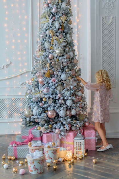 Charmosa loirinha com cabelos encaracolados em um lindo vestido rosa, adorna a árvore de Natal