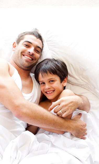 Charmoso pai e seu filho olhando para a câmera na cama