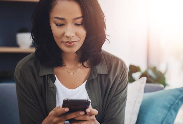 Chatear con una mujer y un teléfono inteligente en el sofá para leer redes sociales o relajarse con internet en el hogar Blog sonreír y persona femenina en la sala de estar o salón para la conexión desplazarse o aplicación móvil para la creación de redes