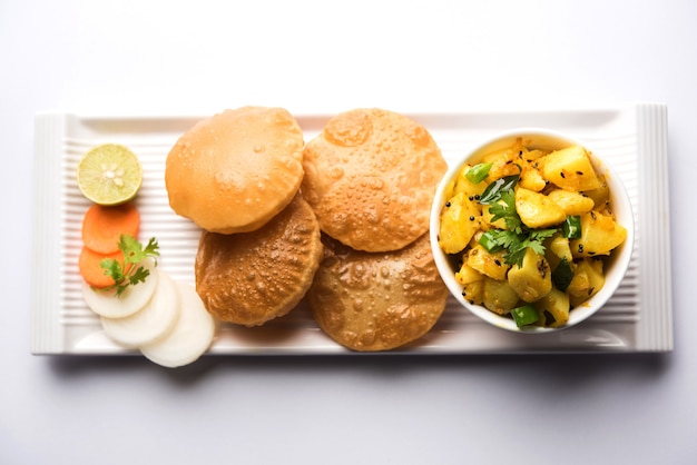 Foto chatpate masala aloo sabzi fry oder bombay kartoffeln serviert mit gebratenem puri oder indischem brot aus weizen in einem teller, selektiver fokus