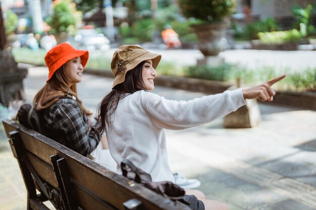 Foto chats turísticos femeninos con el dedo apuntando en la dirección mientras le dice a un amigo que se siente después